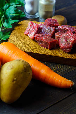 Raw unpeeled potatoes, onions, carrots, and beef on the wooden tableの写真素材