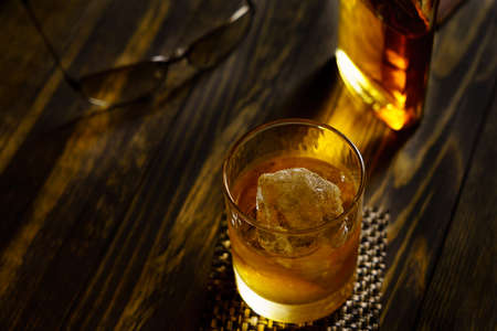 Whiskey in a glass with ice on a wooden tableの写真素材