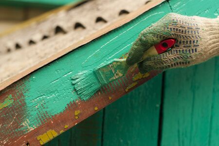 A male hand in work glove with paint brush paints a fragment of the roof of the building. Close-upの写真素材