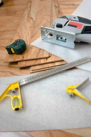 Laminate boards, tape measure, soft backing, corner and electric jigsaw are on the floorの写真素材
