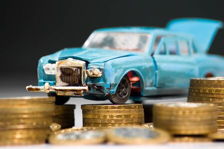 A model of an old car is standing on coins. The concept of expensive maintenance of an old car or its disposalの写真素材