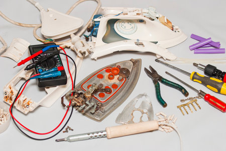 Repair of the iron. Disassembled faulty iron with tools on a white backgroundの写真素材