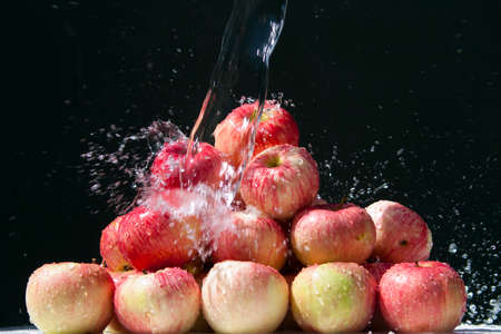 Melba apples. Ripe Melba apples with splashing water are stacked in a heap on a black backgroundの写真素材