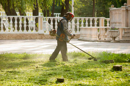 The man takes care of the lawn. One man in protective clothing mows the lawn with a hand-held lawn mowerの写真素材