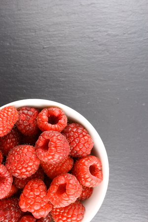 fresh red raspberry fruits in a small white bowl
