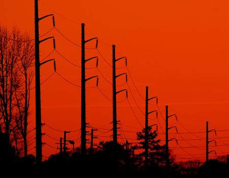 Power transmission lines silhouetted against a bright orange backgroundの写真素材