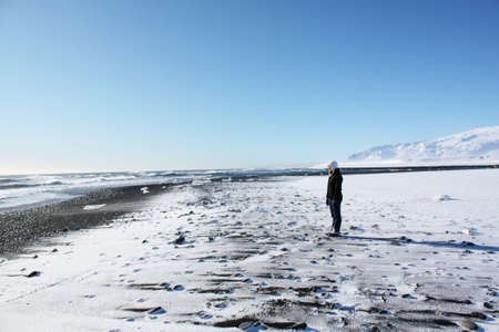 Woman staring at the frozen sea and the back coast in Icelandの写真素材