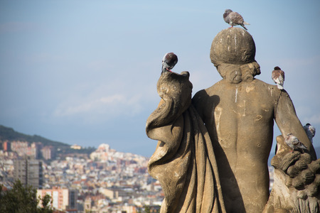 A statue with pidgins on top of Montjuic mountain with the skyline of Barcelona in the backgroundの写真素材