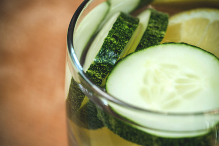Close up of glass of cocktail with lemon and cucumbers on table.の写真素材