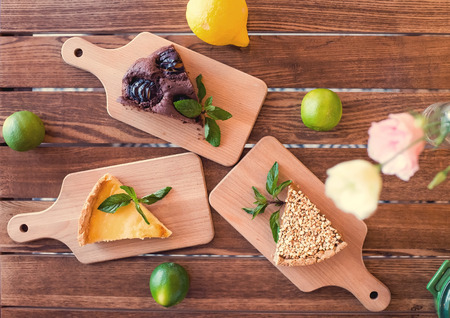Pieces of nut cake, brownie and cheesecake decorated with mint, lemon and lime on wooden table.の写真素材