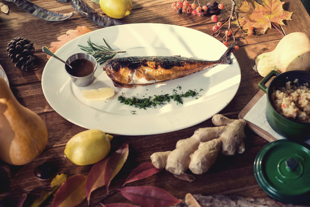 baked fish with rosemary, sauce and lemon on a wooden background.の写真素材