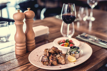 Grilled pork ribs with salad, lemon, sauce and the glass of red wine on the wooden table.の写真素材