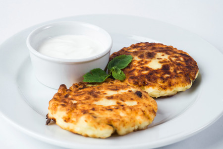 Rustic dessert, cheesecakes on a plate, with sour cream and mint isolated on white.