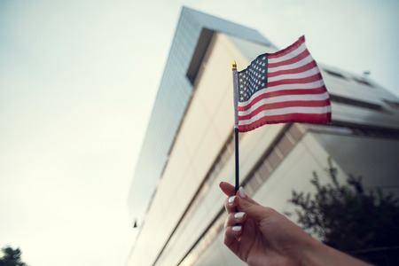Hand holding american flag on the blue sky in the city.の写真素材