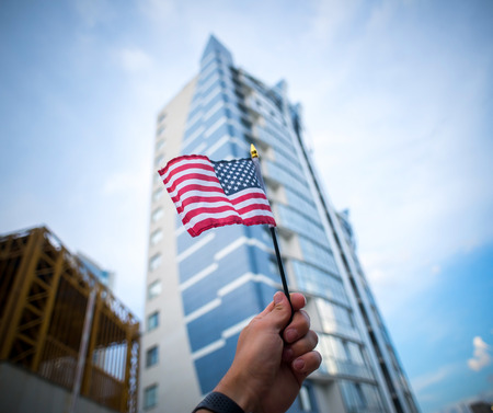 Hand holding american flag on the blue sky in the city.