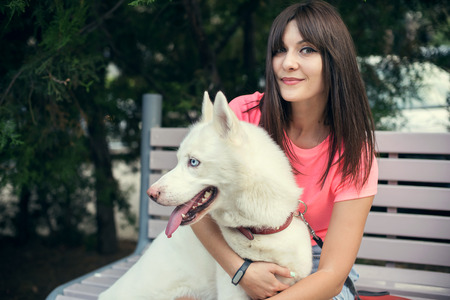 Young girl sitting on the bench and playing with her white husky dog.