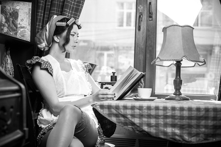 Young woman drinking coffee and reading book sitting indoor in urban cafe.の写真素材