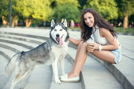 girl drinking ice coffee and playing with her husky dog in the park.の写真素材