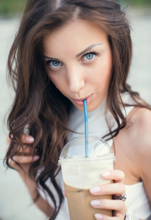 Happy beautiful girl sitting on stairs in park and drinking ice coffee.の写真素材