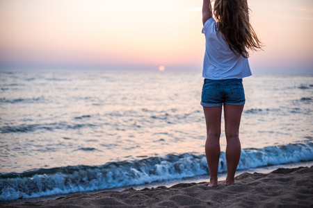 Young woman standing on the stone, looking at sunset over the sea.の写真素材