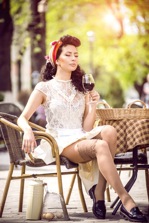 Beautiful young girl with glass of red wine alone in a street cafe.の写真素材