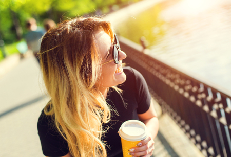 Portrait of a girl in sunglasses with a paper cup of coffee . Shooting at sunsetの写真素材