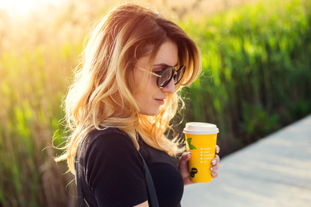 Portrait of a girl in sunglasses with a paper cup of coffee . Shooting at sunset