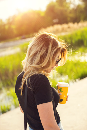 Portrait of a girl in sunglasses with a paper cup of coffee . Shooting at sunsetの写真素材