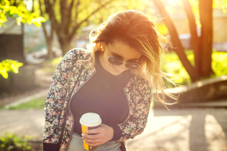 Portrait of a girl in sunglasses with a paper cup of coffee . Shooting at sunsetの写真素材