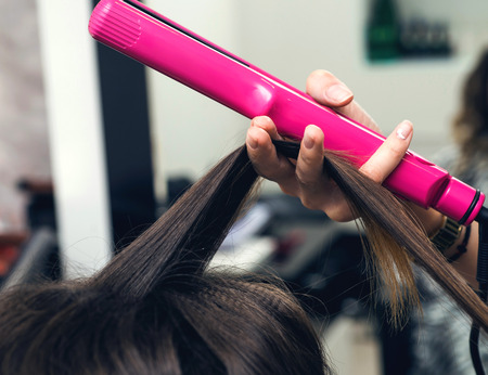 Close-up of a hairdresser straightening long brown hair with hair ironsの写真素材