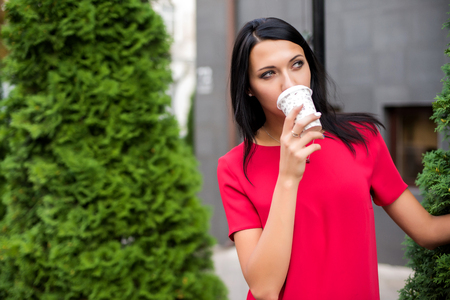 Young stylish woman drinking coffee to go in a city streetの写真素材