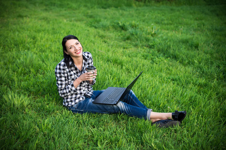 girl lying on the grass and using laptop and typing with coffeeの写真素材