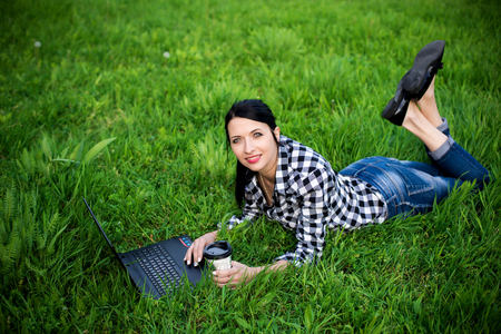 girl lying on the grass and using laptop and typing with coffee.の写真素材