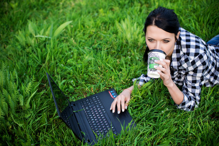 girl lying on the grass and using laptop and typing with coffee.の写真素材