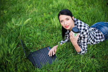 girl lying on the grass and using laptop and typing with coffee.の写真素材