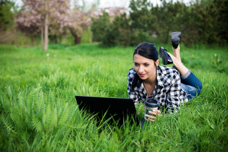 girl lying on the grass and using laptop and typing with coffee.の写真素材