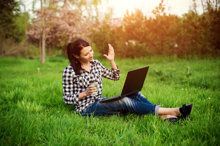 girl lying on the grass and using laptop and typing with coffee.の写真素材
