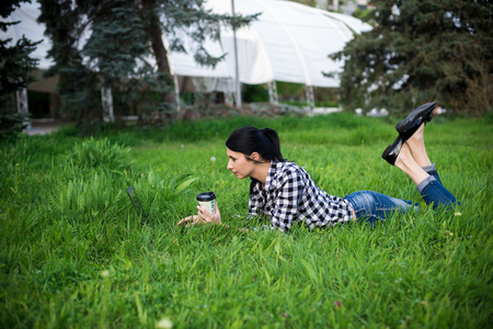 Attractive young woman is lying on grass near a university. She is drinking coffee and relaxing.の写真素材