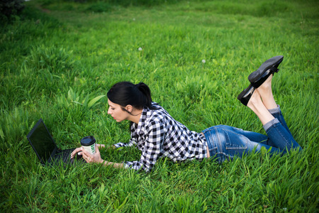 Attractive young woman is lying on grass near a university. She is drinking coffee and relaxing.の写真素材