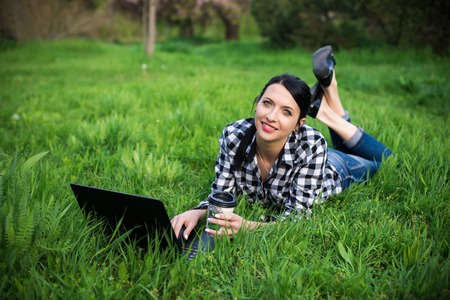 Attractive young woman is lying on grass near a university. She is drinking coffee and relaxing.の写真素材