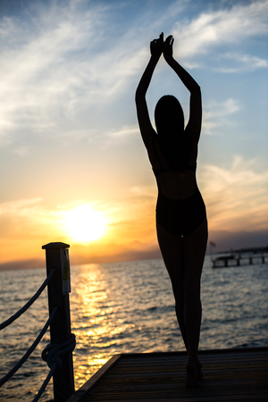 beautiful tan woman in bikini on the pier admiring sunset.の写真素材