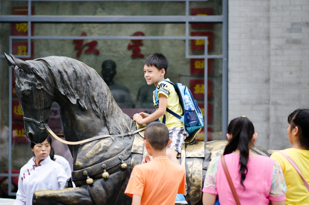Beijing qianmen street-Augest 2015- A boy is enjoying his wonderful holiday,He rode on horseback in bronze ,InBeijing qianmen street Chinaのeditorial素材