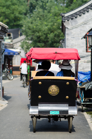 Beijing Houhai alley-Augest 2015- Two tourists sitting on a human tricycle Visit Beijing alley,in BeiJing Chinaのeditorial素材