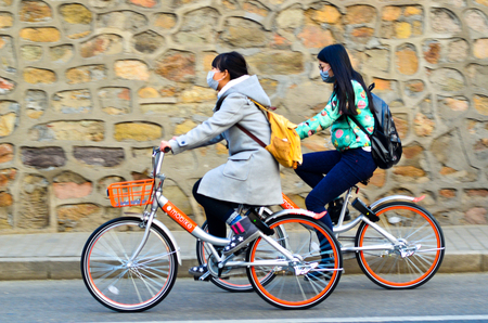 Beijing,China-December 2016-Two girls wearing masks, riding  Mobike  bicycles through the front wall.のeditorial素材