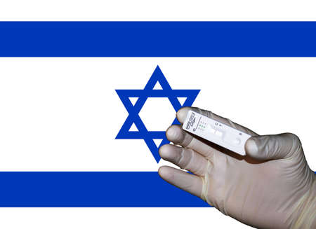 a hand showing a virus quick test in front of an israeli flagの写真素材