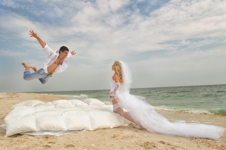Happy Groom flying on bed to his bride on the beachの写真素材