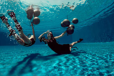 Underwater shoot of flying two women with black balloonsの写真素材