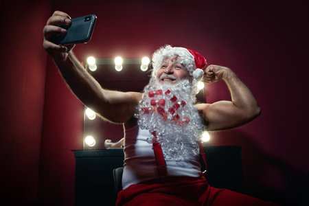 Narcissistic Santa Claus is making selfie with mobile phone camera in a dressing roomの写真素材