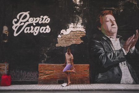 Beautiful woman changing her shoes to her sneakers while walking down the street in a small Spanish townの写真素材