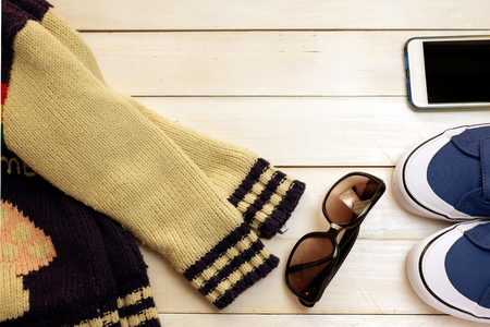 Winter clothes ;blue sneaker ,glasses ,sweaters and smartphone on white wood board background ,concept idea for traveling in winterの写真素材